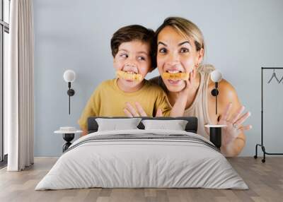 Mother and son enjoying and eating a Latin American snack called tequeños, funny expressions on their faces Wall mural