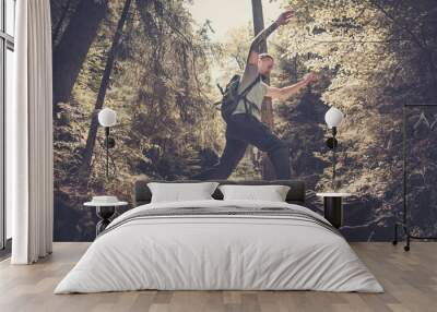 Man hiker jumping across stream in mountain forest Wall mural