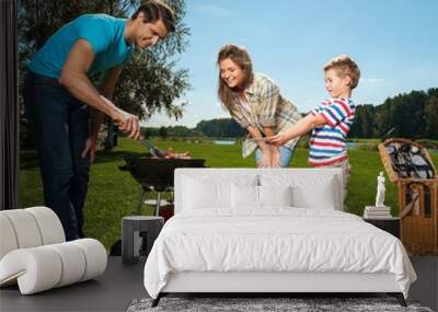 Young family preparing sausages on a grill outdoors Wall mural