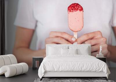 close-up of the hands of a girl in a white t-shirt with a pink cake on sticks Wall mural