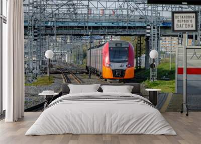 A modern high-speed red train on a section of the Moscow Central Circle Line. Comfortable city rail public transport. Summer sunny day. The inscription in Russian means: Stop of the first car. Wall mural