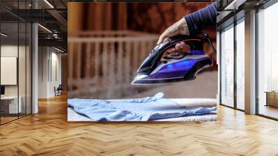 Closeup female hand ironing clothes on the table. Puffs of hot steam break out of the iron. Dark blurred background. Wall mural