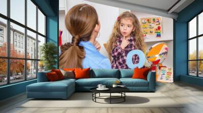 Young girl  in speech therapy office. Preschooler exercising correct pronunciation with speech therapist. Wall mural