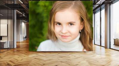 Portrait of a beautiful little girl close-up in a white sweater on a background of green textural natural background Wall mural