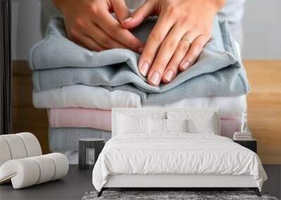 A person's hands folding a stack of clean, freshly laundered clothes on a wooden surface Wall mural