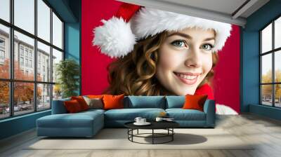 A young Caucasian woman with long curly brown hair wearing a Santa hat, smiling and looking away from the camera against a red background Wall mural