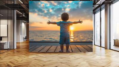 Rearview of a little toddler boy with spread arms walking on a wooden deck towards the sunset over the sea or ocean water. Child happiness, infant kid at summer holiday or vacation alone Wall mural