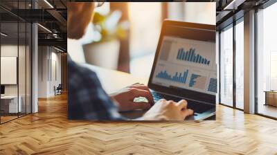 Young businessman wearing glasses, sitting in office, and looking at the company charts and graphs, corporate analytics on a laptop or notebook screen. Male employee working, job workplace Wall mural