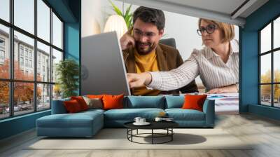 Colleagues in a business meeting discussing project details, collaborating over a laptop. Professional teamwork, consultation, and planning in an office environment. Wall mural