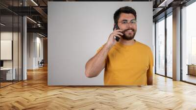 Oh, great news! Smiling young casual man talking on the phone on the grey background. Isolated. Network, phone call and man with a smile, conversation and model isolated on a transparent background. Wall mural