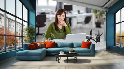 Beautiful smiling Caucasian businesswoman sitting in modern office and using laptop. Wall mural