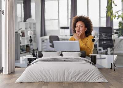 beautiful smiling mixed race businesswoman dressed casual sitting in office and using laptop. Wall mural