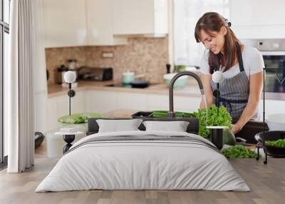 Cheerful attractive Caucasian woman in apron washing salad in kitchen. Dinner at home concept. Wall mural