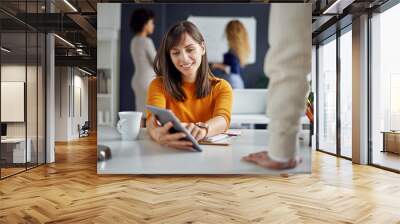 Young woman is talking to his colleague in the office, two women discuss behind her in front of whiteboard Wall mural