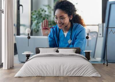 Attractive afro female doctor talking while explaining medical treatment to patient through a video call with laptop in the consultation. Wall mural