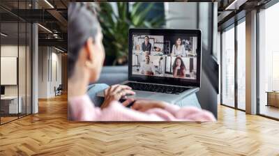 Back view of beautiful woman speaking on video call with diverse colleagues on online briefing with laptop on sofa at home. Wall mural