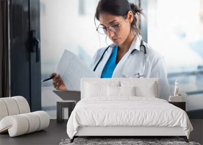 Beautiful female doctor reviewing medical documents while standing in the consultation. Wall mural