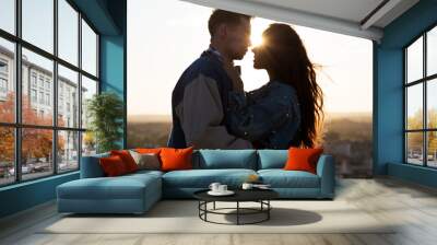 Beautiful young couple in love standing at a building rooftop at the sunset. Wall mural