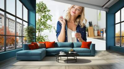 Beautiful young woman eating yogurt at home. Wall mural