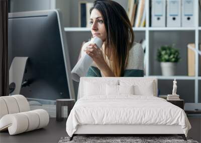 Concentrated young business woman working with computer while drinking coffee in modern startup office. Wall mural