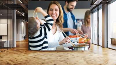 Cute little boy having fun with his young mother while eating spaghetti on kitchen at home. Wall mural