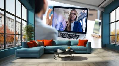 female employee waving and speaking on video call with her colleague on online briefing with laptop  Wall mural