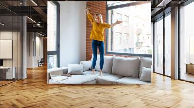 Funny woman listening to music with smartphone while dancing on the couch in the living room at home. Wall mural