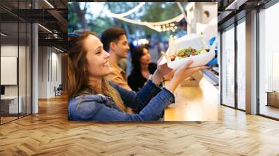 Group of attractive young friends choosing and buying different types of fast food in eat market in the street. Wall mural