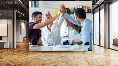 Group of successful smart business team celebrating good job while holding up their right hands on coworking place. Wall mural