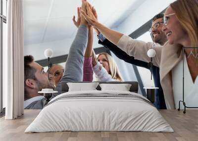 Group of successful young businesspeople holding up their right hands on coworking place. Wall mural