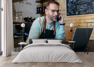 Handsome mature owner bakery working while analyzing report for order delivery with laptop in a pastry shop. Wall mural