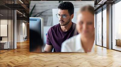 Handsome young entrepreneur using the laptop while his colleagues working together in the office. Wall mural