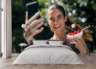 Happy woman eating healthy breakfast while taking a selfie with her smartphone in the garden Wall mural