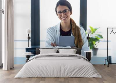 Happy young female doctor smiling and looking at camera while digital tablet and standing in the consultation. Wall mural