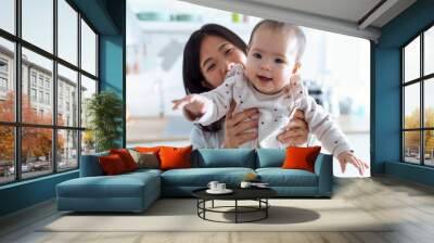 Happy young mother with her baby daughter looking at camera in the kitchen at home. Wall mural