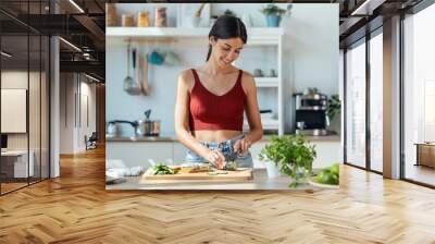 Healthy young woman cutting fresh vegetables while cooking healthy food in the kitchen at home. Wall mural