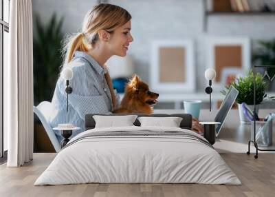 Lovely little dog looking the laptop while her beautiful owner working with him in living room at home. Wall mural