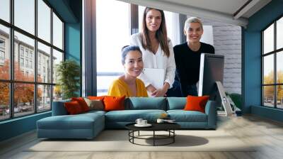 Modern three entrepreneur women looking at camera while working in the office. Wall mural