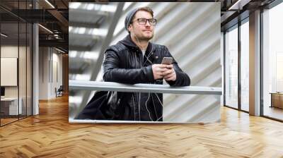 Modern young man listening to music with mobile phone in the street. Wall mural