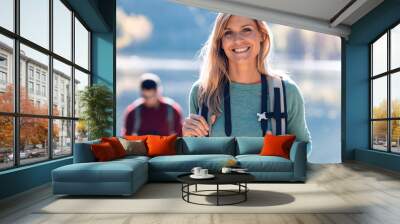 Pretty young female hiker smiling while looking at camera in front of lake. Wall mural