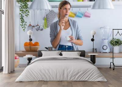 Pretty young woman eating yogurt while standing in the kitchen at home. Wall mural