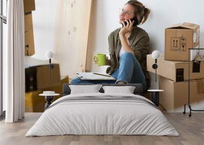 Pretty young woman talking on her mobile phone while sitting on her new house. Wall mural