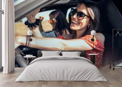 Pretty young women singing while driving a car on road trip on beautiful summer day. Wall mural