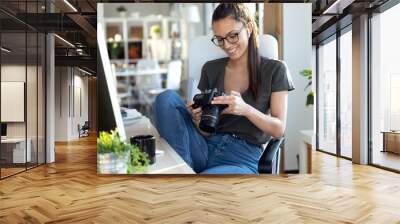 Professional young photographer reviewing the photos she has taken with the camera while sitting in the studio. Wall mural