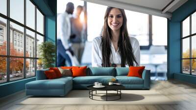 Smiling young businesswoman looking at camera while standing in the coworking space. Wall mural