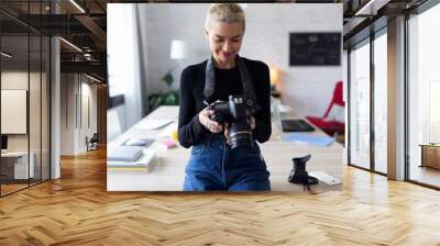 Smiling young entrepreneur woman reviewing her last photographs in the camera while sitting in the office. Wall mural