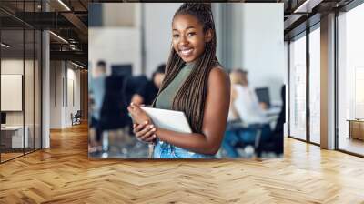 Smiling young entrepreneur woman using her digital tablet while standing and looking at camera in a coworking place. Wall mural