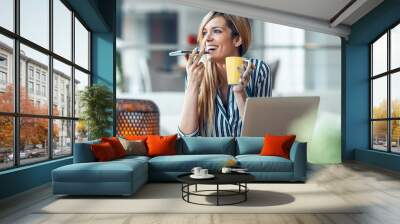 Smiling young woman sending audio message with her smart phone while drinking coffe in the office at home. Wall mural