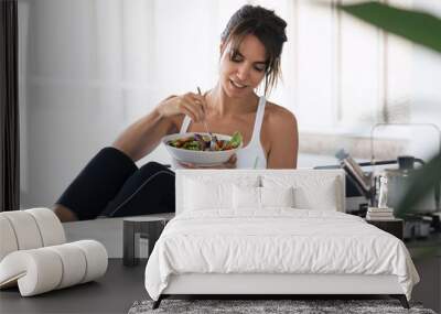 Sporty young woman eating salad and drinking fruit juice in the kitchen at home. Wall mural