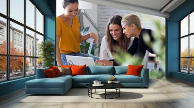 Three modern businesswomen talking and reviewing the latest work done on the computer in a joint workspace Wall mural